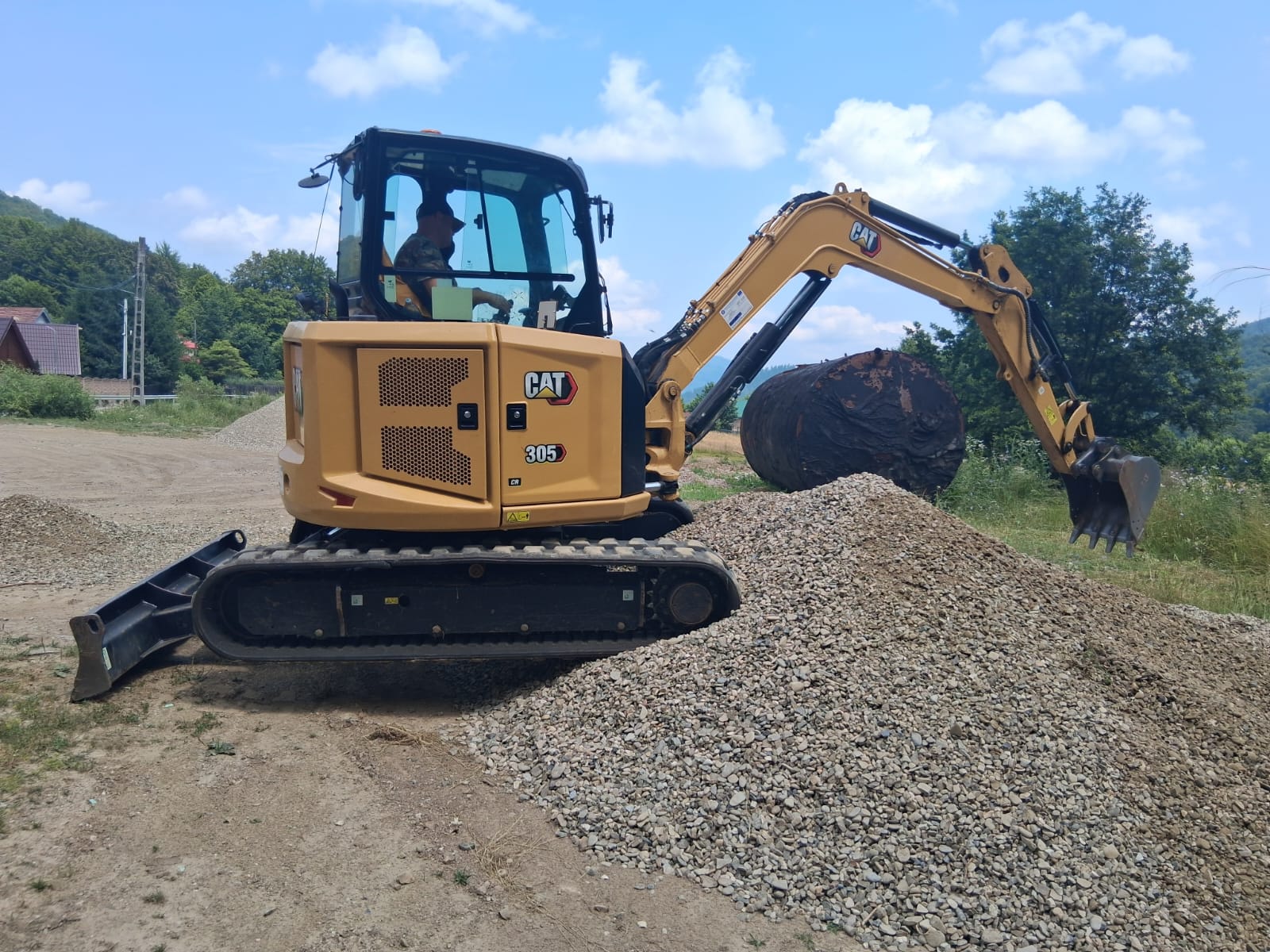 Miniexcavator Caterpillar 305 CR la lucru lângă grămadă de pietriș